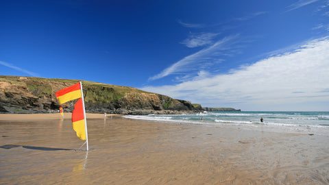 A photo of Gunwalloe Beach at low tide with RNLI lifeguard flags