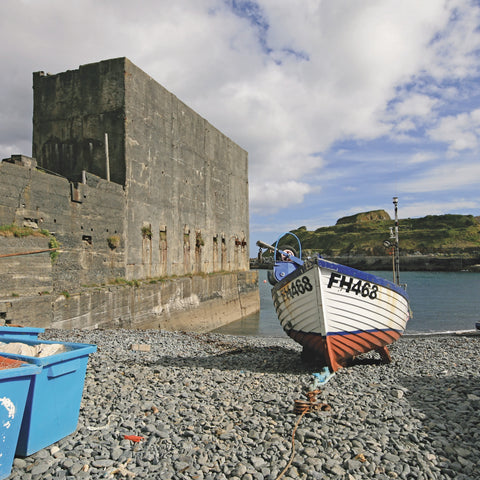 Photo from Friendly Guides Lizard Guidebook of fishing boat pulled up on the shingle beach at Porthoustock on the Lizard Peninsula in West Cornwall. West of England quarry in the background.