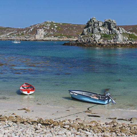 Photo from Friendly Guides Isles of Scilly Guidebook showing boats in Kitchen Porth on Bryher, Isles of Scilly. Looking over New Grimsby Sound to Cromwell's Castle and King Charles' Castle on Tresco.