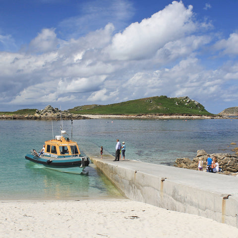 Photo from Friendly Guides Isles of Scilly Guidebook showing the Lightning ferry landing at Lowertown (Hotel) Quay on St Martin's, Isles of Scilly. In the background Yellow Carn and Great Hill on Tean.